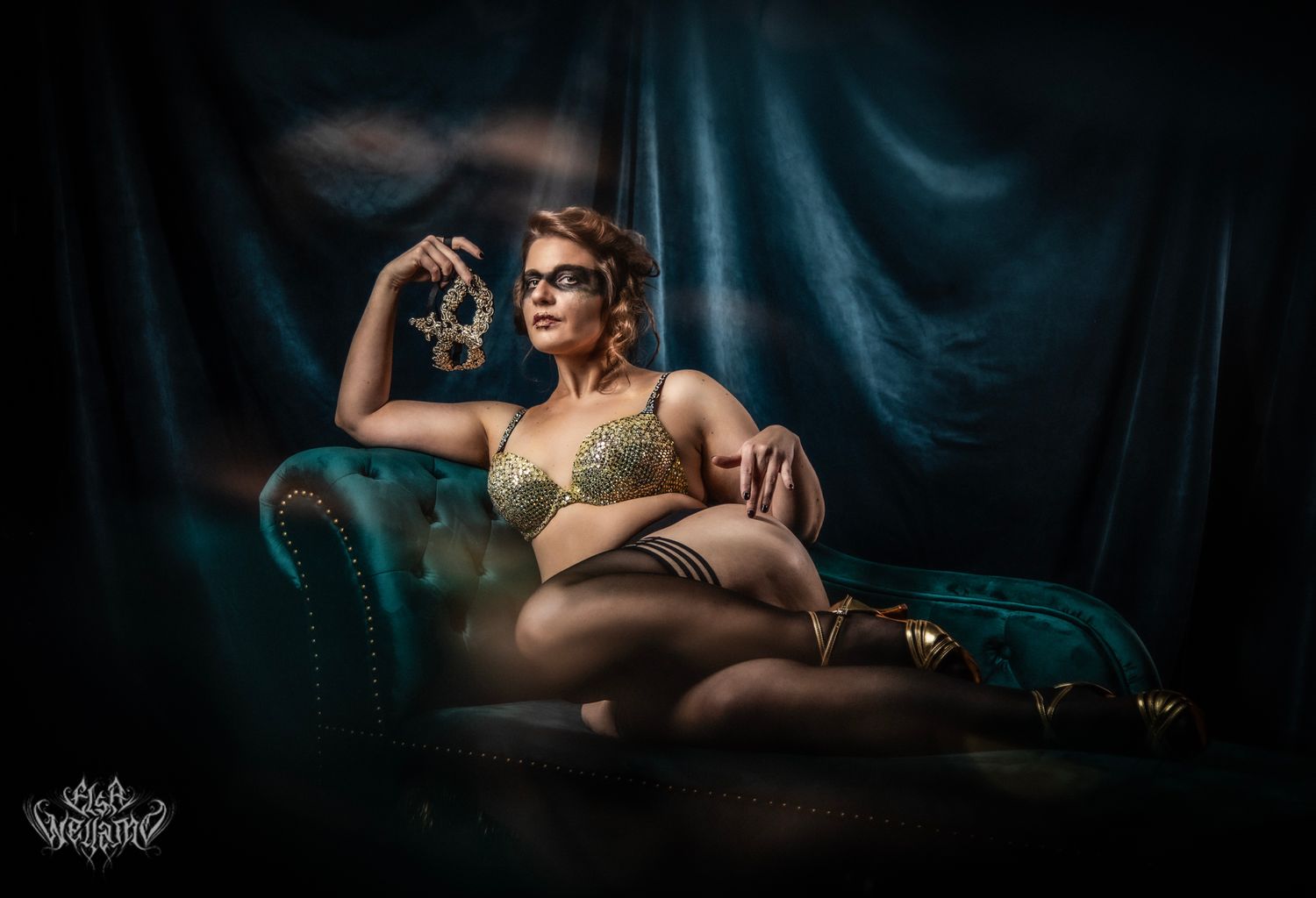 Dramatic boudoir portrait on teal velvet chaise lounge with moody lighting against dark backdrop.