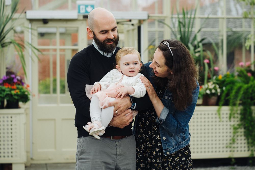 Family shares tender moment together in garden setting with plants and flowers.