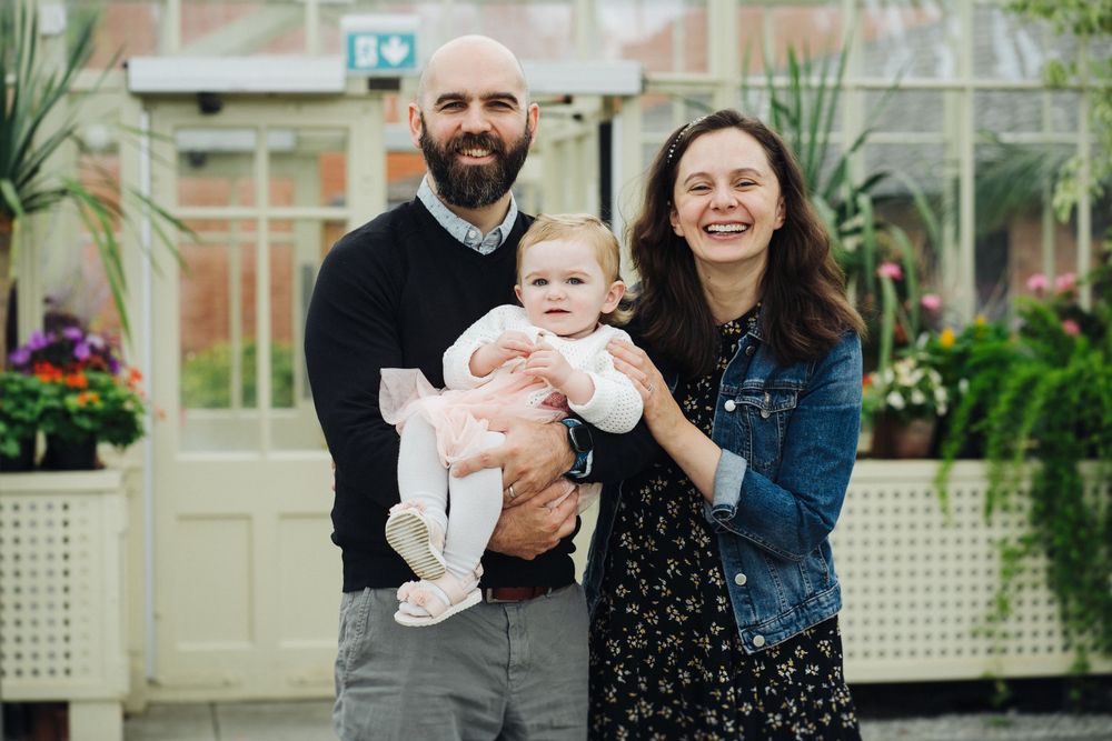A happy family shares joyful moments together in a greenhouse setting with natural lighting and greenery.