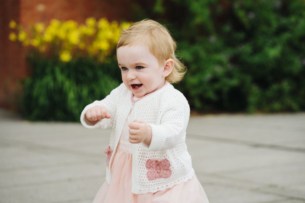 A child in a white and pink outfit plays with bubbles in a sunny outdoor setting.