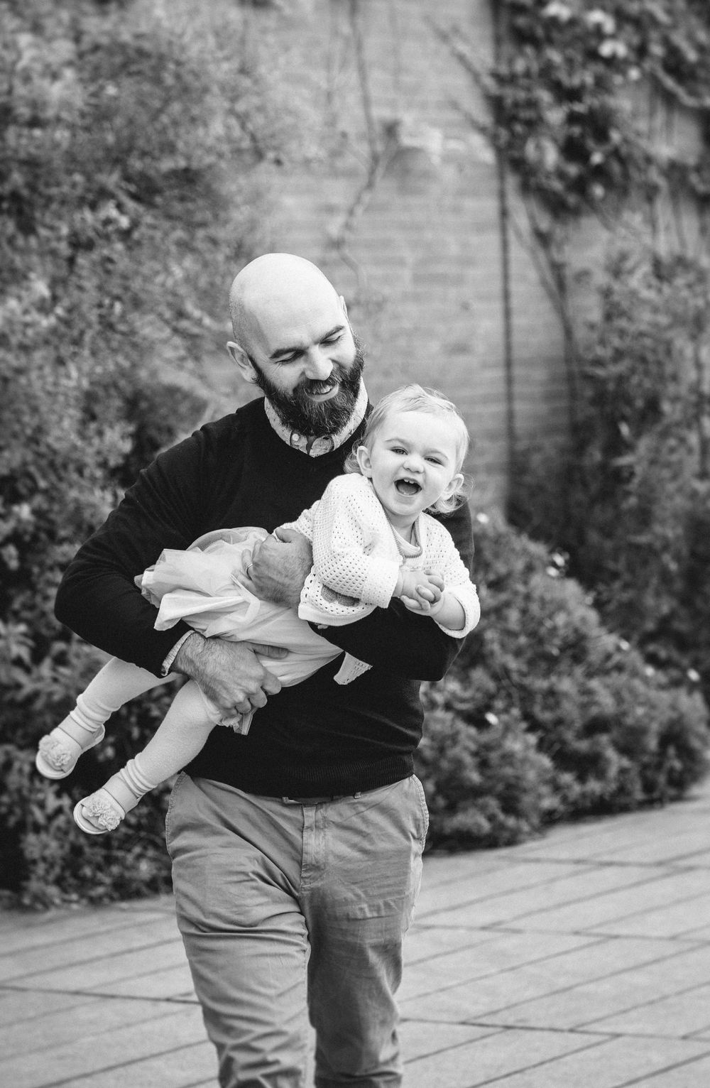 Black and white photo sequence showing playful interaction between adult and baby in outdoor garden setting.