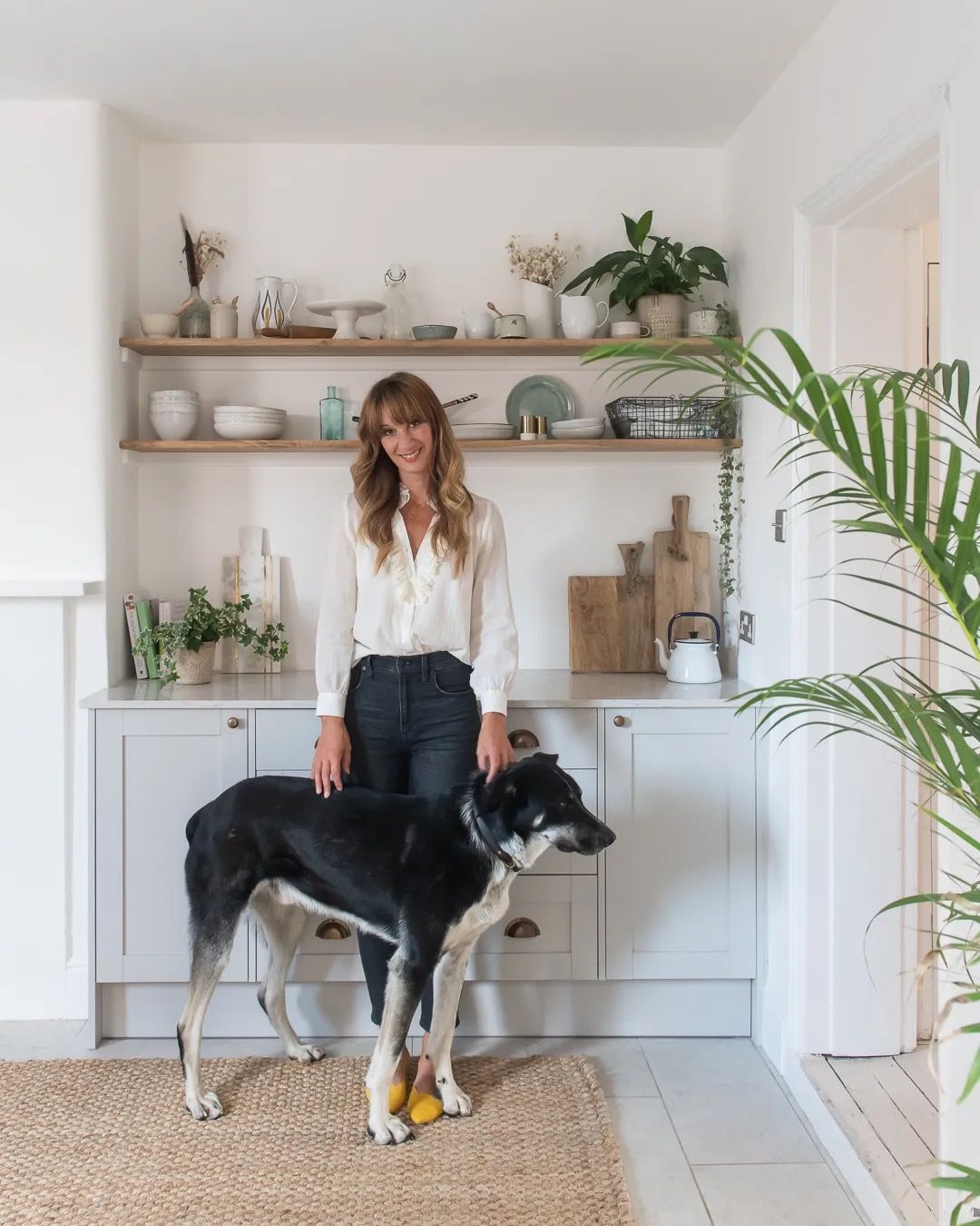 A woman standing in a light, modern kitchen with a large dog at her feet.