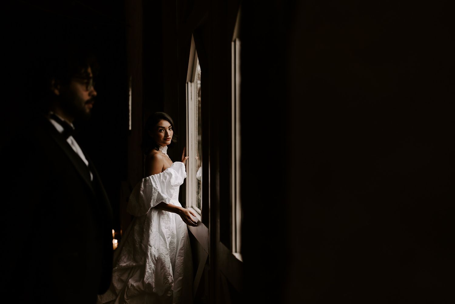 A person stands in dramatic lighting by a window, creating a moody silhouette against the dark background.