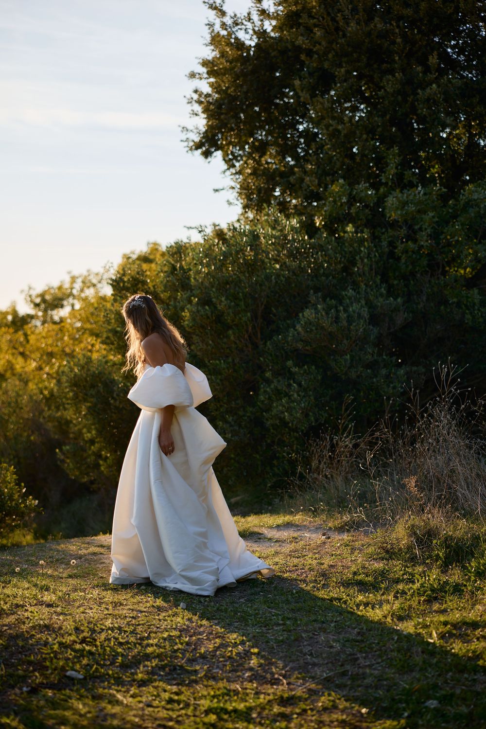 A white wedding dress flows gracefully along a hilltop path at golden hour.