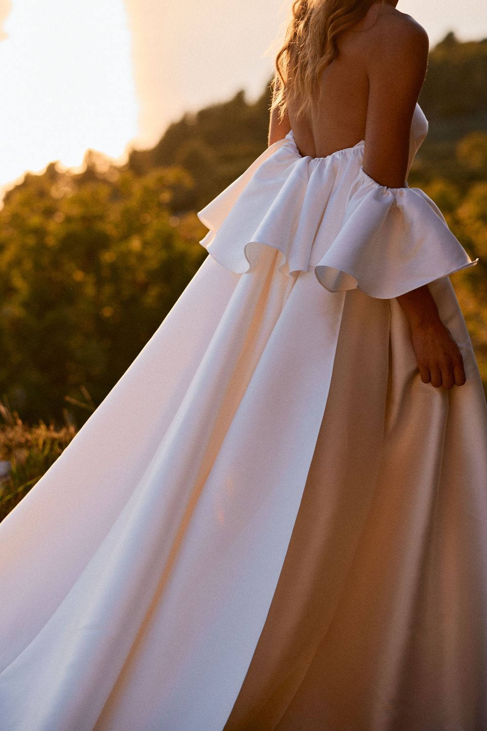 Elegant white wedding dress with ruffled details photographed during golden hour.