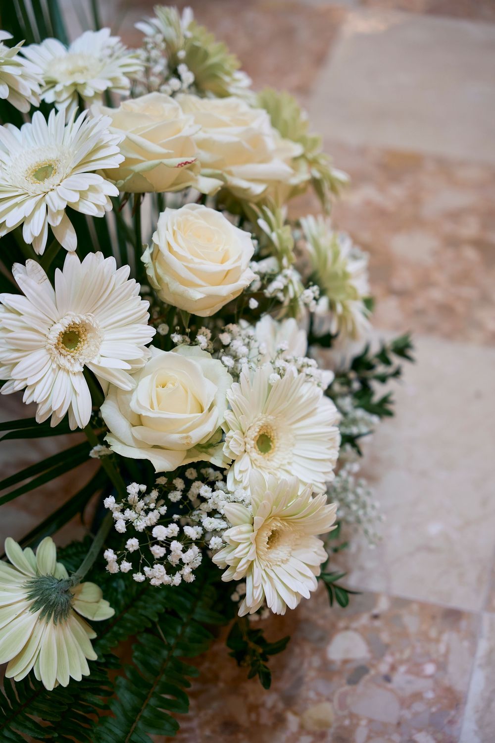 Elegant white floral arrangement with cream roses, gerbera daisies and baby's breath against a textured background.