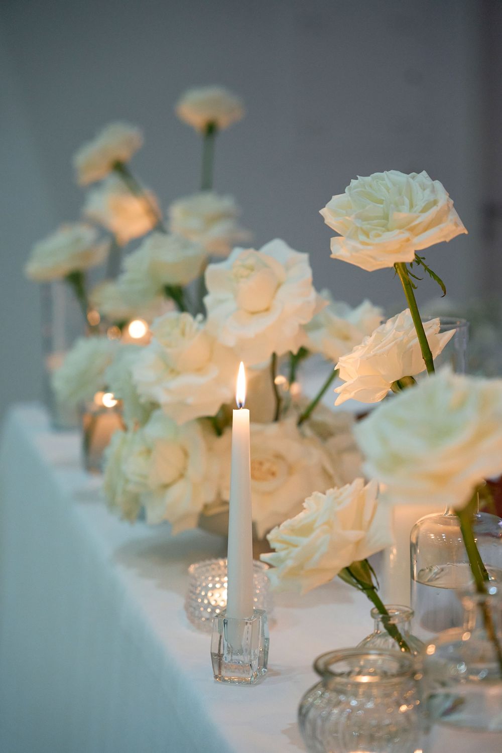 White roses and lit candles create an elegant table setting with glass vases in a romantic atmosphere.