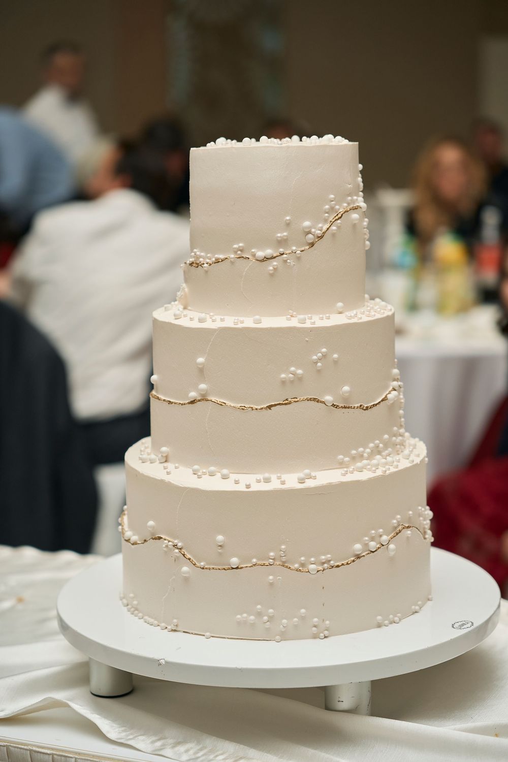 Elegant three-tier white wedding cake with delicate pearl detailing and cascading design.