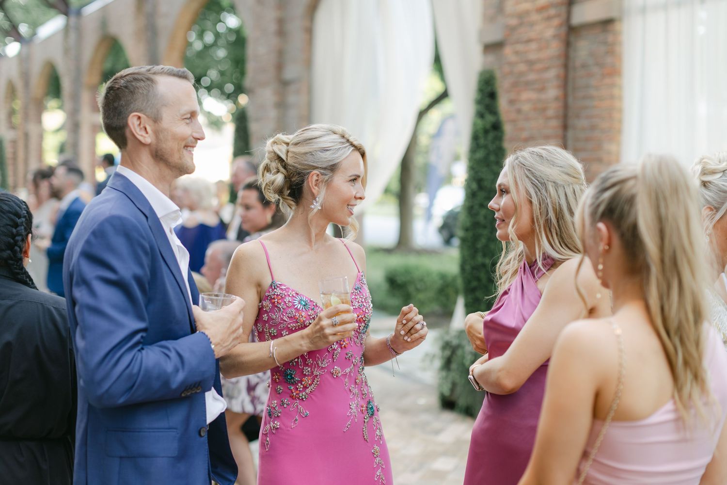 Wedding party members share laughter and conversation during outdoor celebration in formal attire.