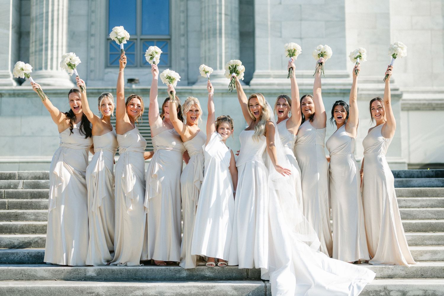 Wedding party wearing white dresses poses on grand stone steps in a celebratory sequence of photos.