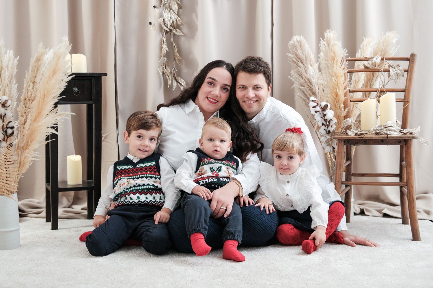 Holiday family photo with matching outfits sitting on floor with festive decorations.