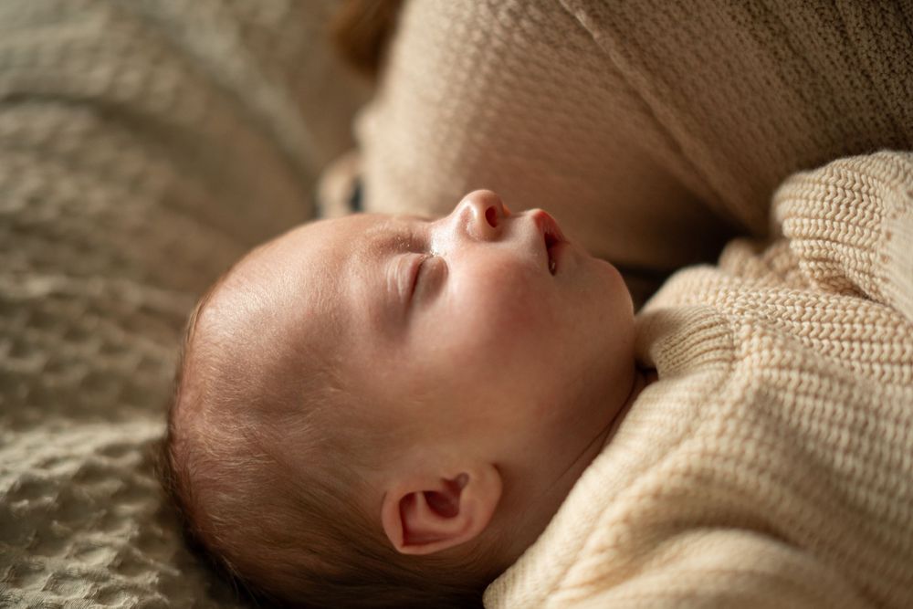 A series of side profile photos showing a sleeping baby in a cream-colored knit outfit against a textured backdrop.
