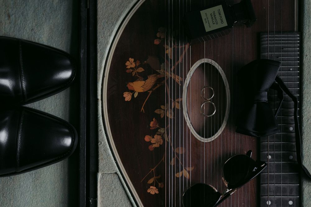 Overhead view of an acoustic guitar with decorative floral pattern and dress shoes on dark background.