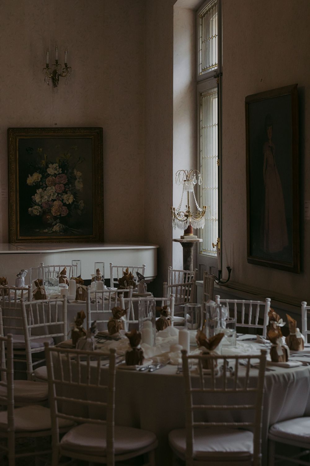 Elegant dining room interior with white chiavari chairs and formal table settings in soft, moody lighting.