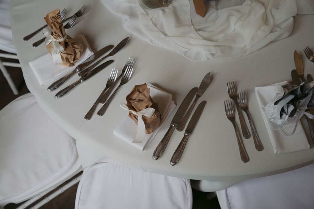 A rustic place setting with silverware and brown paper napkins arranged on a white tablecloth.
