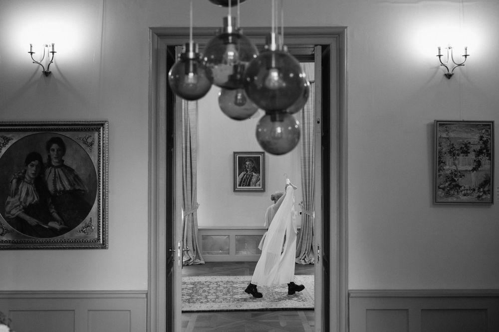 Black and white interior photograph showing framed artwork on walls with a chandelier and decorative elements.