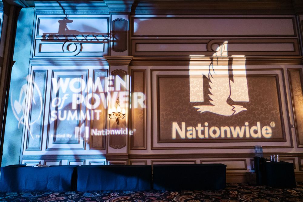Blue illuminated Power of Many logo and Nationwide insurance company signage projected on a dark wall.