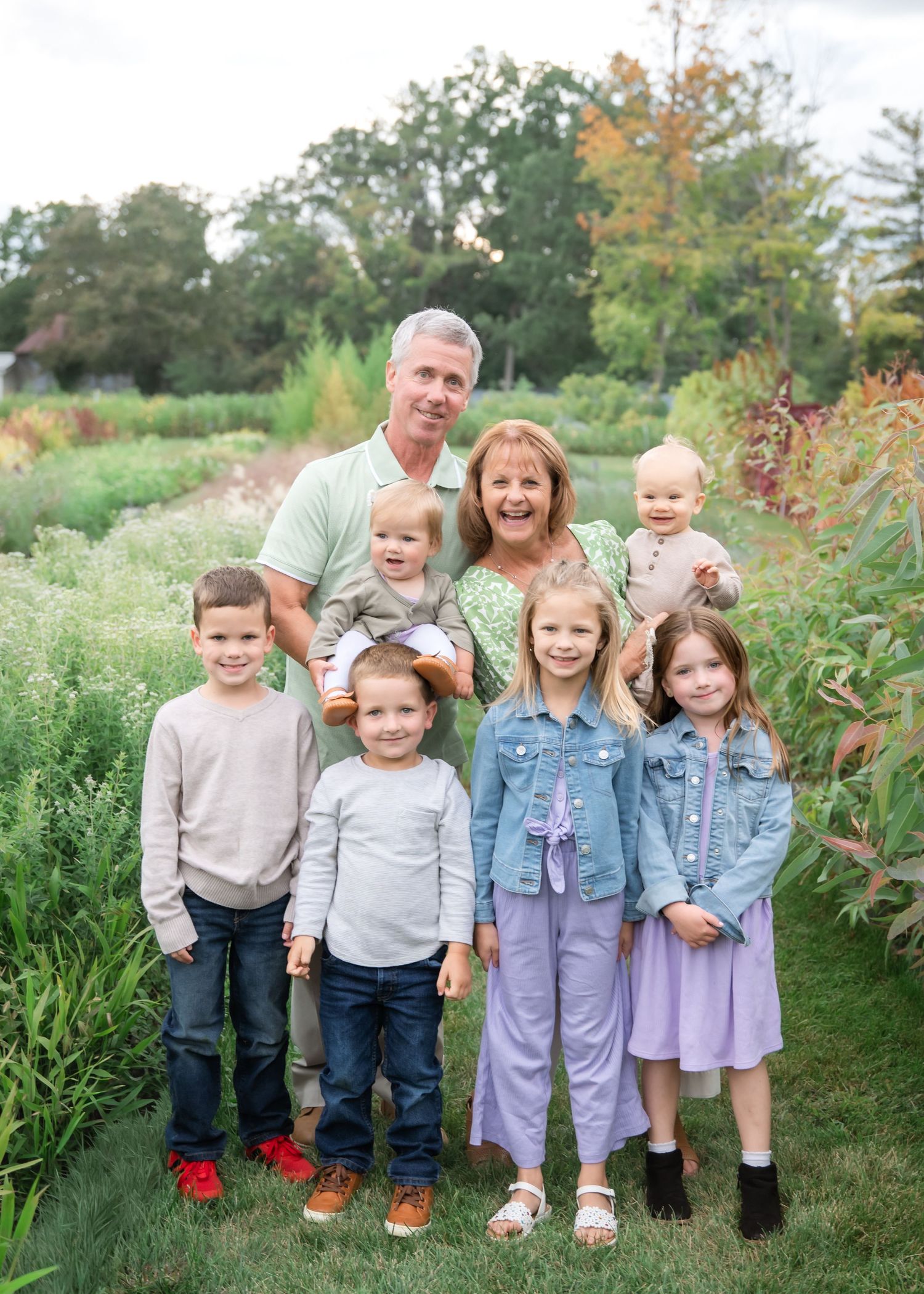 A group of children stand together outdoors in coordinating outfits against a natural backdrop of greenery and flowers.