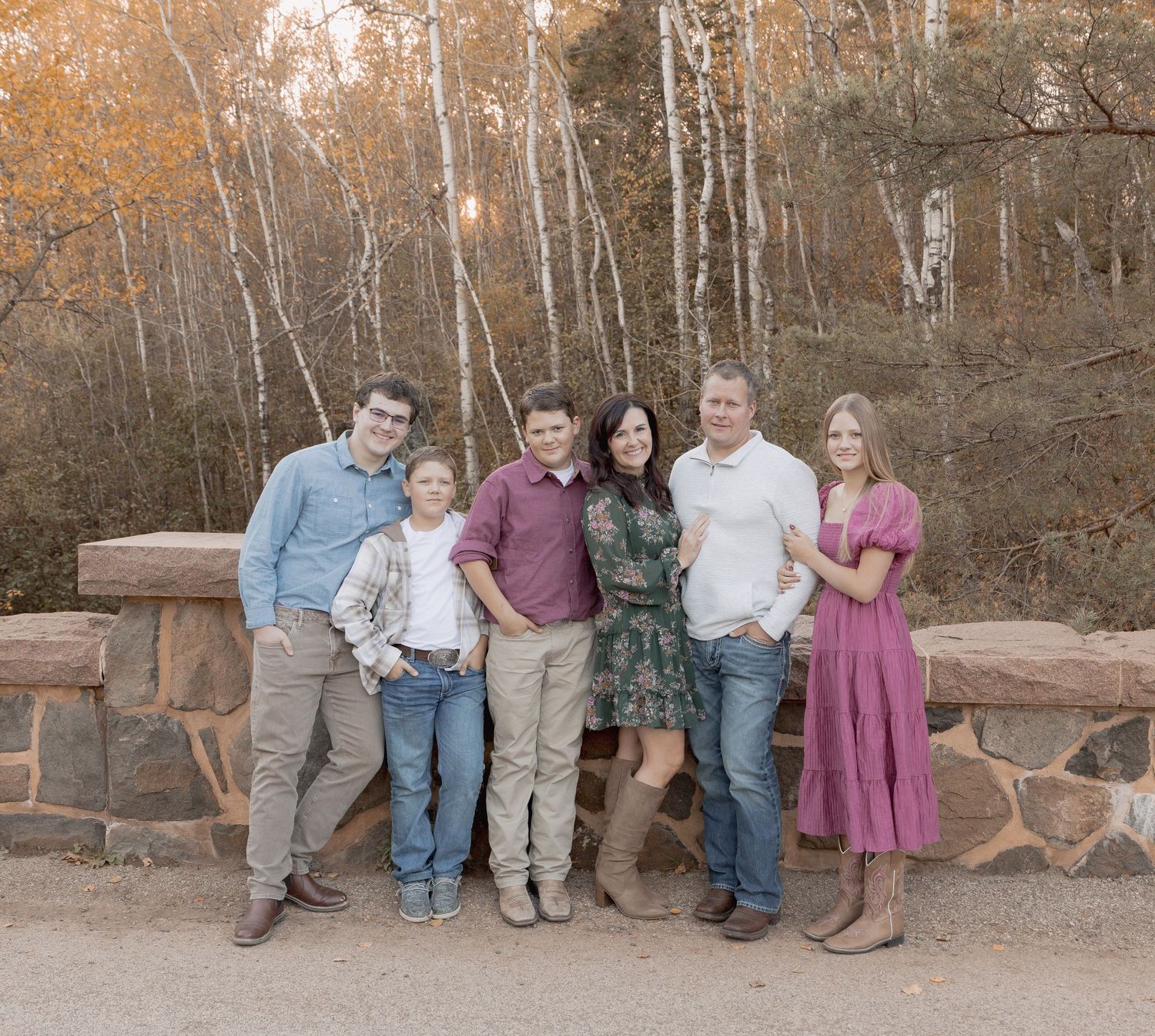 A group of people sitting together on a stone wall during an autumn outdoor family photo session.