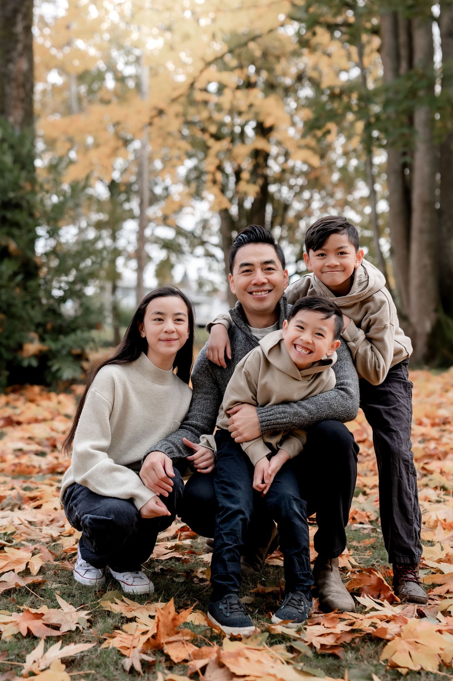 A casual family photo session showing people sitting together on autumn leaves in coordinated beige outfits.