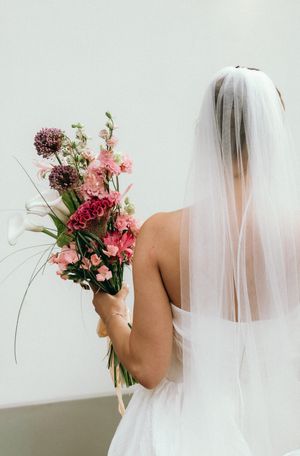 A bridal bouquet of pink and red flowers held against a white veil in an artistic series of shots.