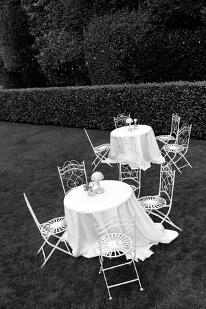 Black and white photo of elegant white garden tables and chairs set up for an outdoor reception.