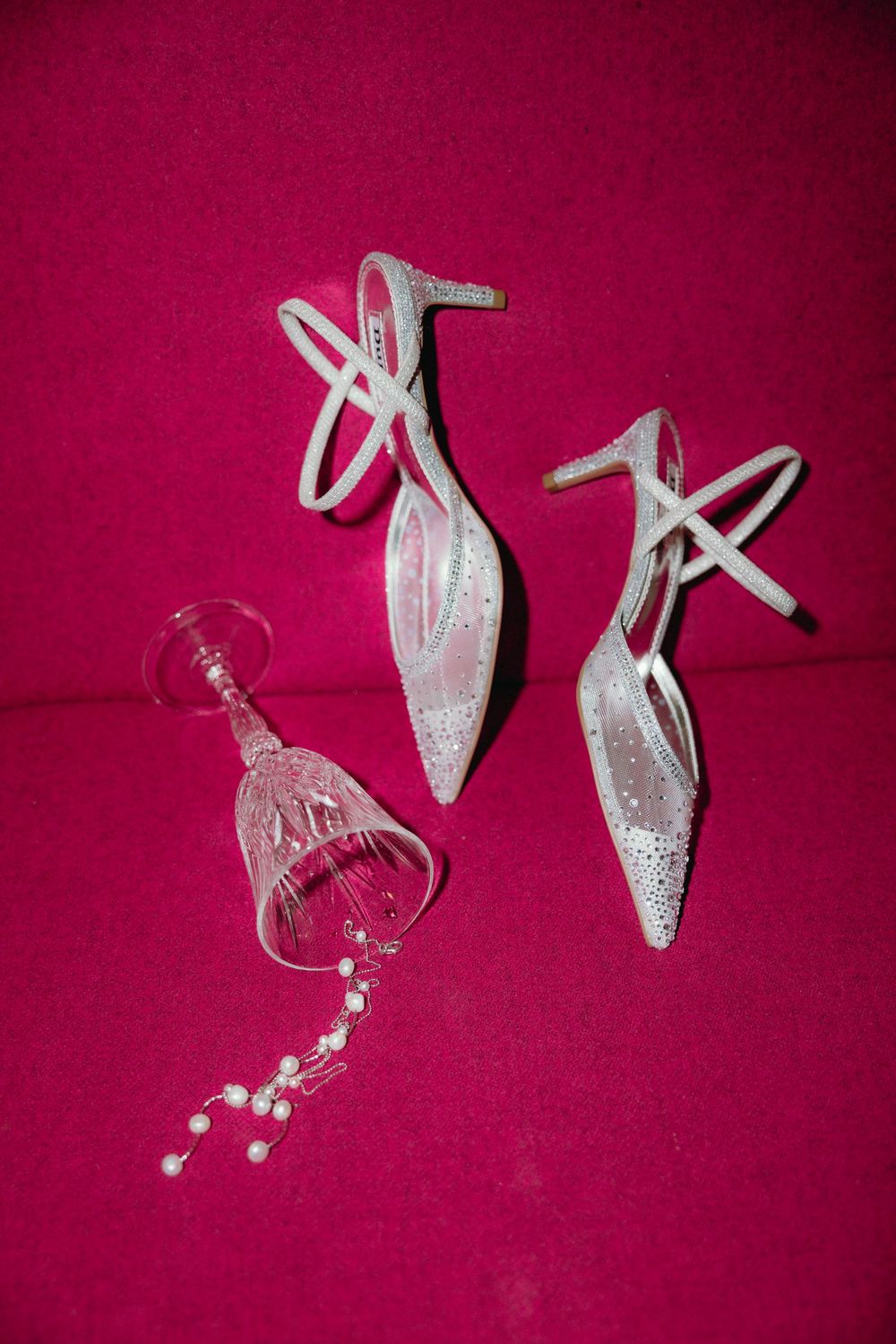 Sparkly white bridal shoes arranged on a pink background with jewelry.