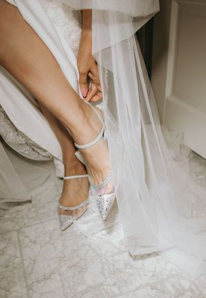 Close-up of bride putting on sparkly white wedding shoes.