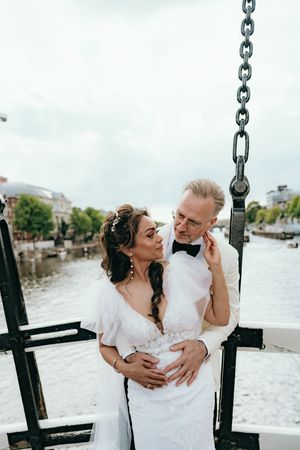 Couple embraces near waterfront chain railings during wedding photoshoot.