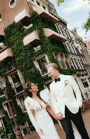 Wedding couple poses in front of ivy-covered historic building with striped awnings.