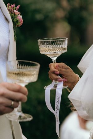 Elegant champagne glasses with white ribbons being held during a wedding celebration.