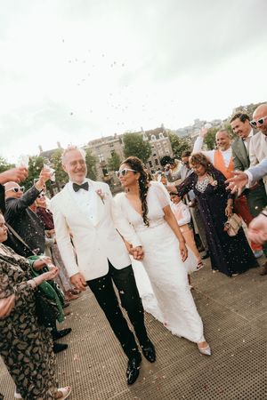 Wedding guests throwing confetti as newlyweds walk through on outdoor pathway.