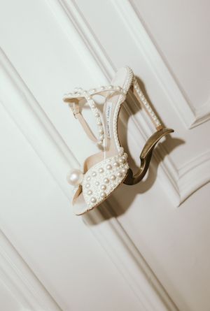 Pearl-embellished bridal heels photographed against a white paneled wall.