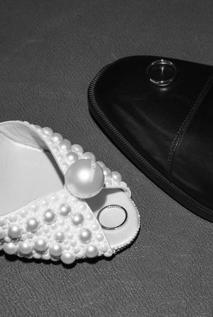 Black and white still life of pearl-decorated wedding shoes with rings.