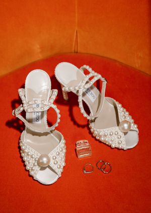 White bridal shoes with pearl embellishments displayed on an orange background.