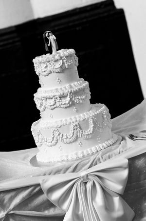 Elegant white wedding cake with intricate piping details and satin bow decoration.