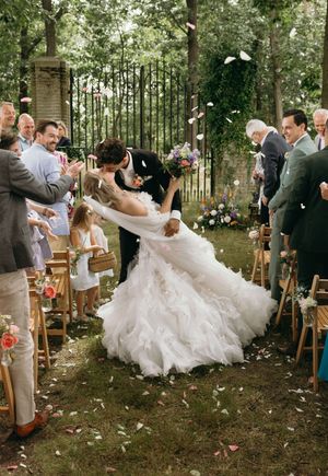 Wedding couple dips during outdoor forest ceremony with guests watching.