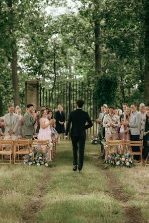 Outdoor wedding ceremony in a wooded setting with wooden chairs and floral decorations lining the aisle.