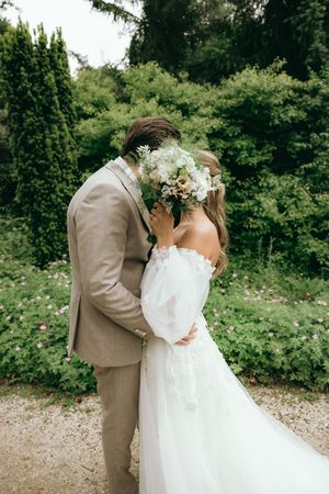 Romantic wedding couple embracing in a lush garden setting with the bride wearing an off-shoulder gown.