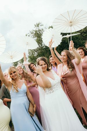 Wedding party holding white parasols outdoors in pastel colored dresses.
