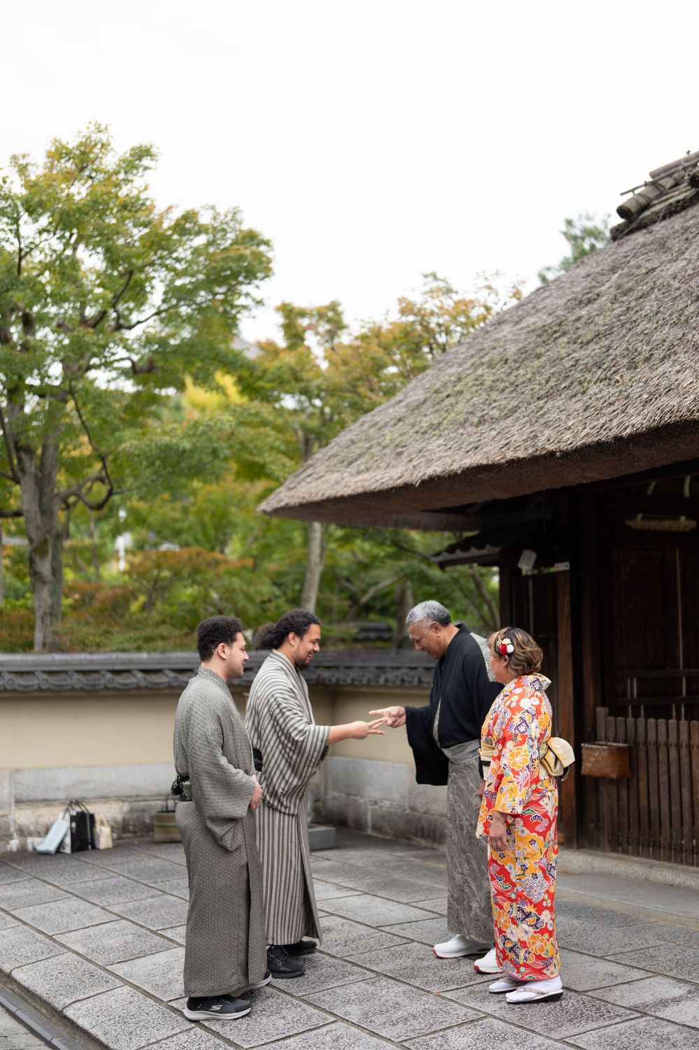 Family in traditional Japanese kimono greeting outside a thatched roof building in Kyoto.