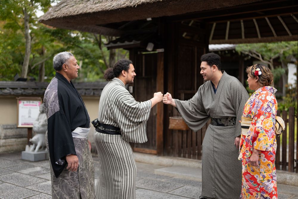 Group of four in colorful kimono shaking hands outside traditional Japanese architecture.