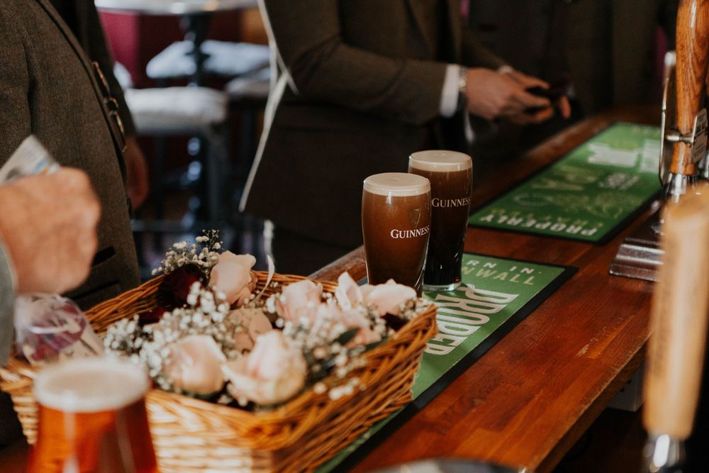 Two pints of Guinness on a wooden bar beside a wicker basket with white wedding flowers.