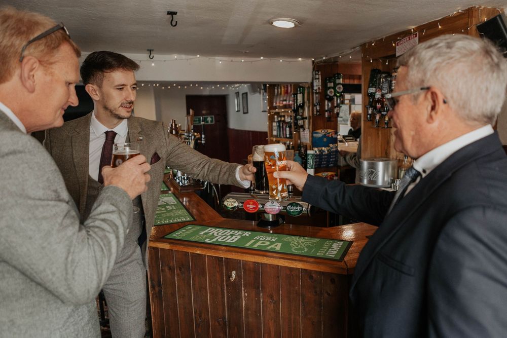 Three men in suits raising glasses in a toast at a traditional wooden pub bar.
