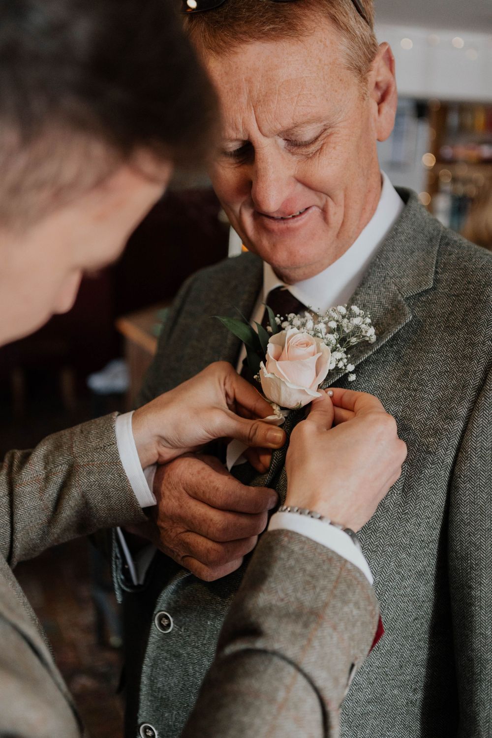 Smiling older man in grey tweed suit having a pink rose boutonniere pinned to his lapel.