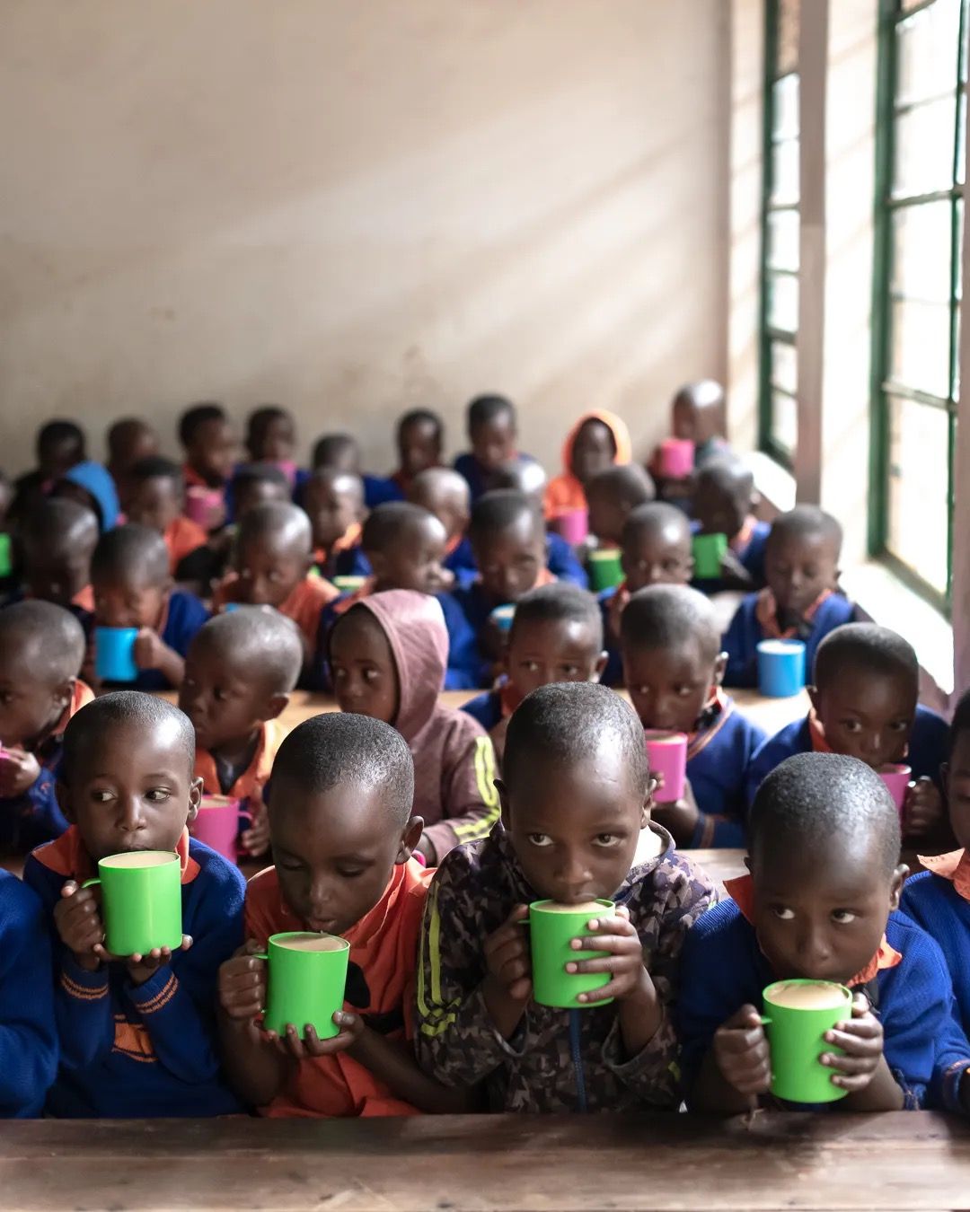 Young children sit with food containers during a school nutrition programme supporting health and early learning.