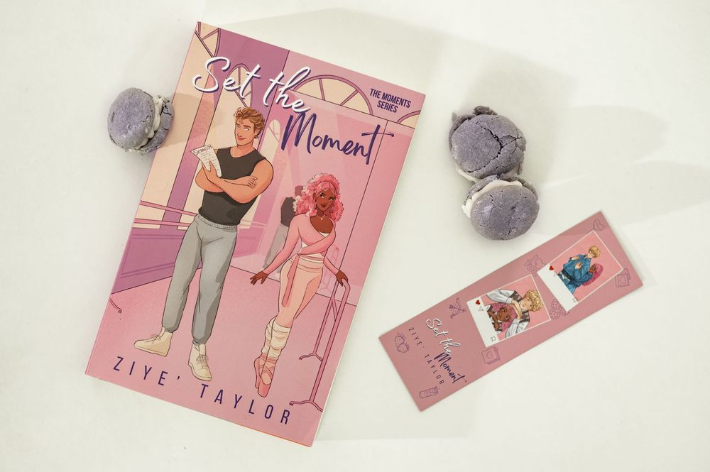 A pink book titled 'First Time Mommy' with a bookmark and purple bath bombs arranged on a light background.