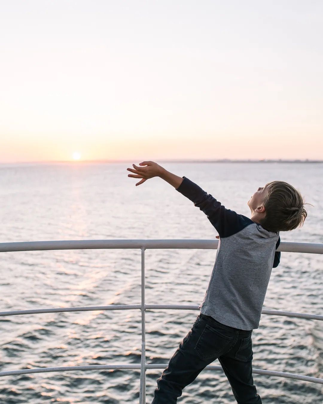 Boy dancing on a ferry deck at sunset.