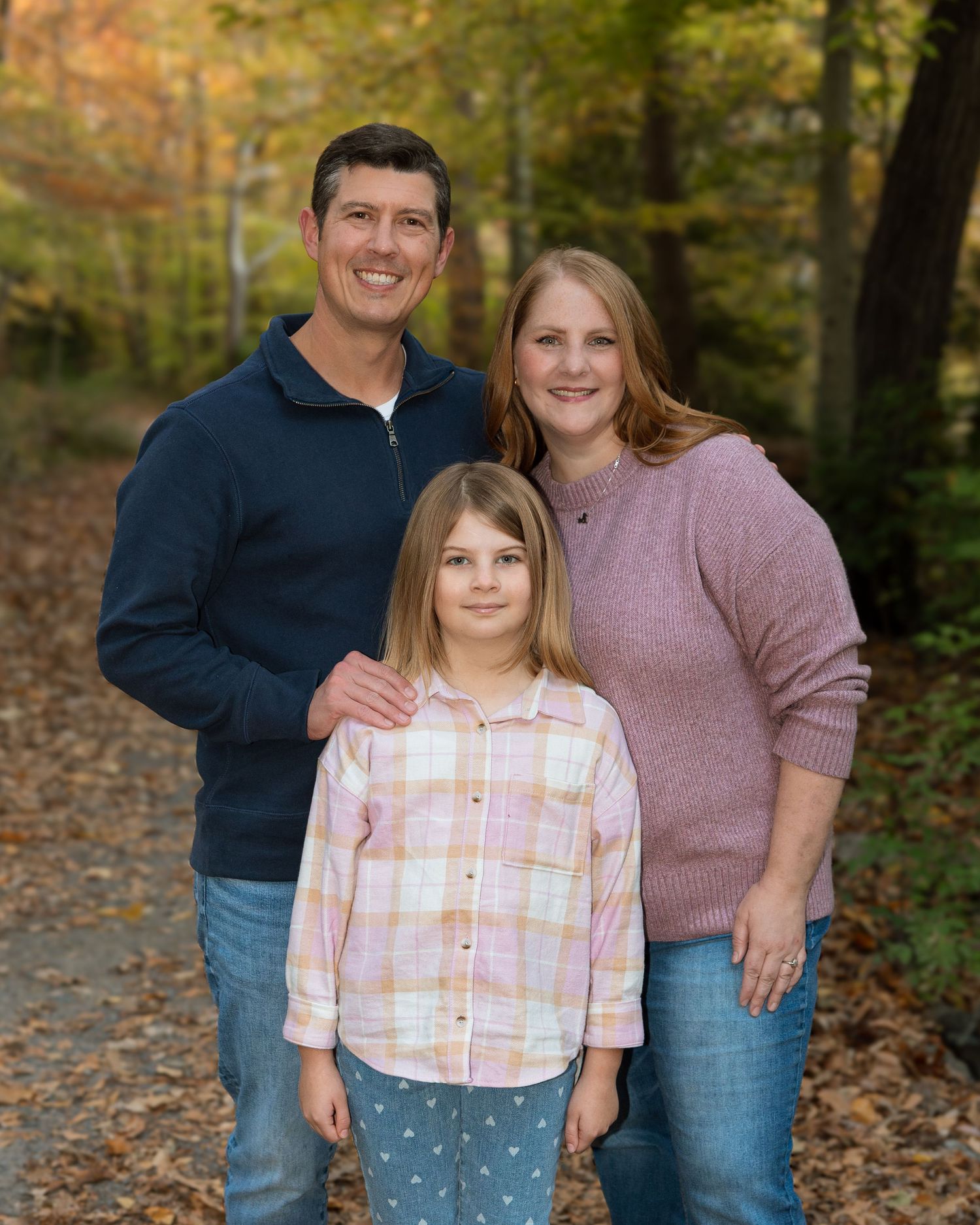 Family portrait of parents and daughter on wooded path — relaxed outdoor family photography