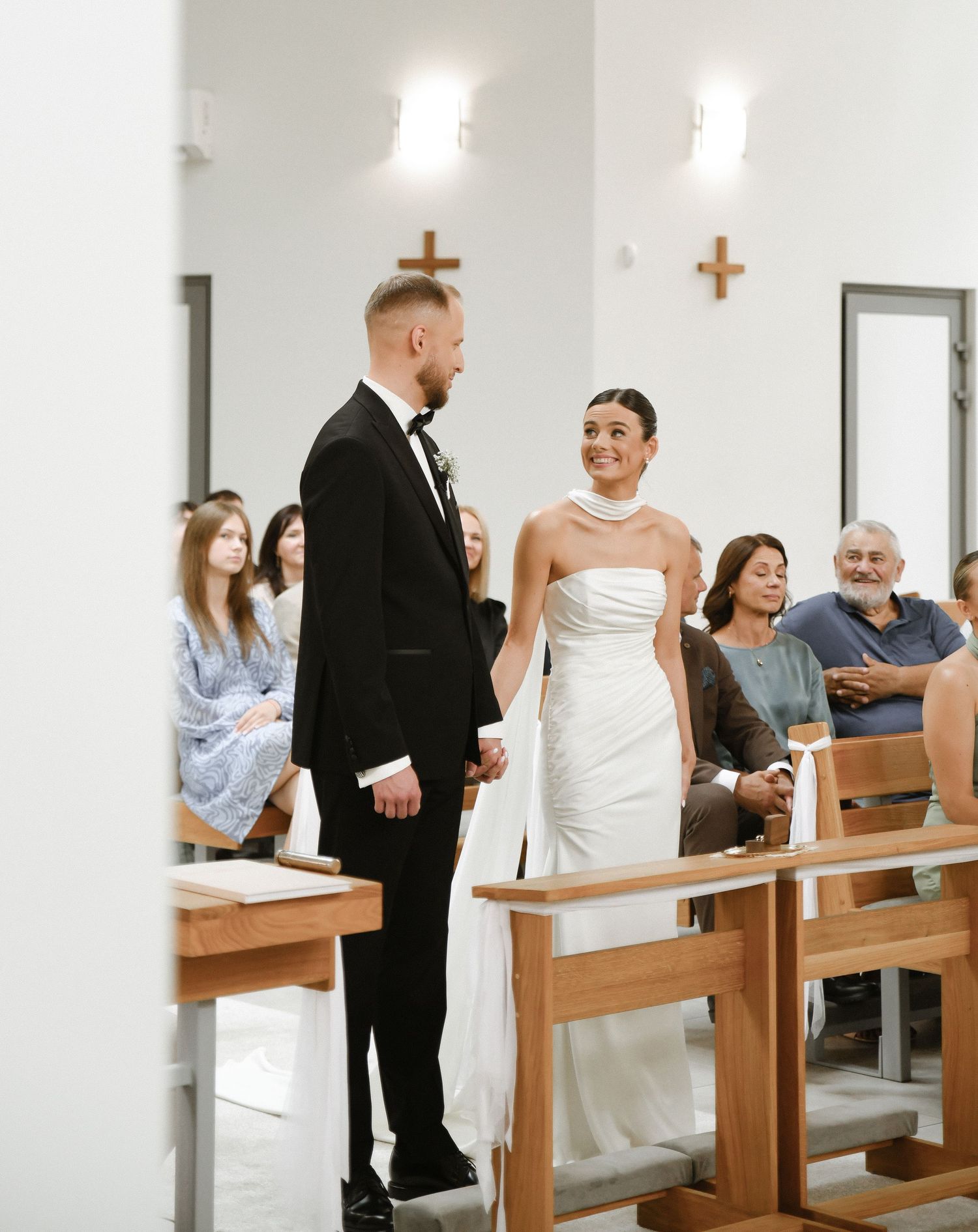 Wedding ceremony inside a modern minimalist church with wooden pews and white walls.